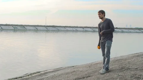 Man near the Gulf throws up fruit in slow motion. Male throws an orange at sky. Stock Footage 72595598