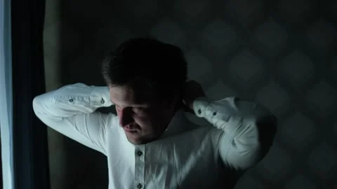Man near a window adjusting his shirt collar and putting on a tie Stock Footage 325728657
