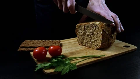 A man nervously cuts grain bread on a cutting wooden board. Stock Footage 99655046