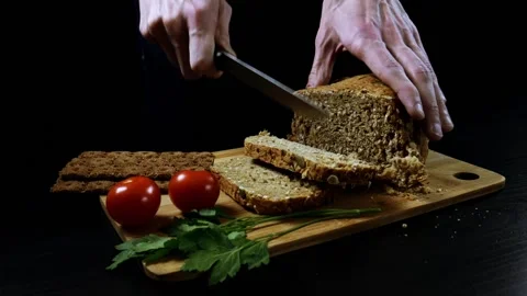 A man nervously cuts grain bread on a cutting wooden board. Stock Footage 99655496