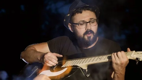 A man at night sitting by the fire plays the guitar. Stock Footage 116467757