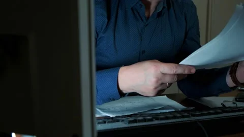 A man at night at work in the office at his desk sorting through documents Stock Footage 149075180