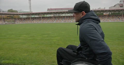 A man with non-functioning legs sitting in a wheelchair at the stadium looks Stock Footage 154255695