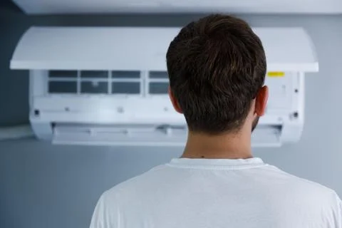 Man Observing Air Conditioning Unit While Standing in Room: A Detailed Focus on Stock Photos