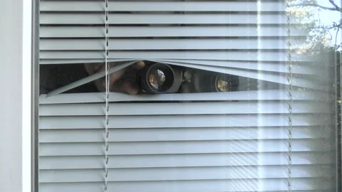 A man is observing with binoculars through the blinds in the window. Stock Footage 141243849