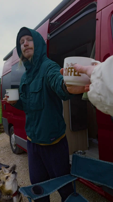 Man offering coffee mug from campervan during mountain camping trip Stock Footage 336631571