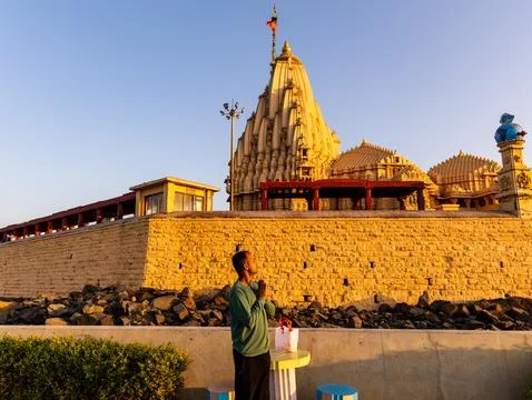 Man offering prayer with folded hands facing somnath temple at golden hour Stock Photos