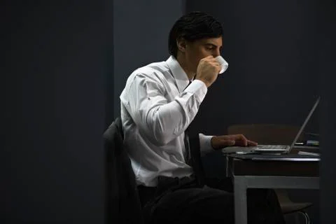 Man in office drinking coffee, working late Stock Photos