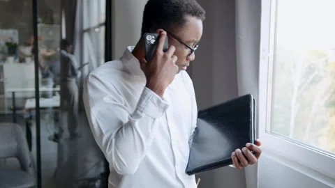 A man in an office is engaged in a heated discussion on his smartphone. He's 스톡 동영상 335753055