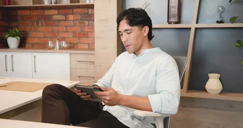 Man in office sitting in task chair, tapping tablet, checking messages, smiling, Stock Footage 339959155
