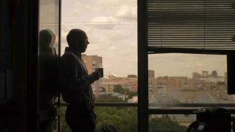 Man in office standing in the window and drink Stock Photos