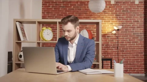 A man in the office is typing something into a laptop then look into the frame. 動画素材 194363584