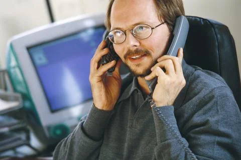 Man in office using cell phone and landline phone at same time Stock Photos