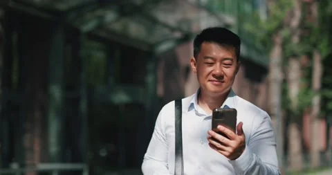 Man office worker, browsing smartphone during a walk on a sunny city street Stock Footage 204920809