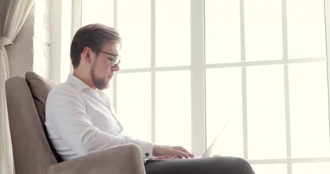 Man office worker in glasses is typing message on laptop in office, side view. Vídeos de archivo 132100672