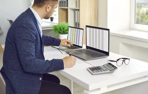 Man in office working with big data and databases using two laptops and excel Foto stock