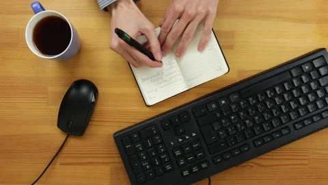 A man in the office writes tasks for the day in the diary on a wooden table Stock Footage 101840351