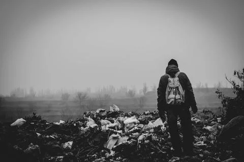 A man in old clothes and with a backpack stands against the background of a l Stock Photos