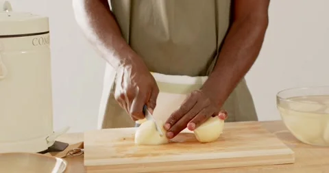 Man in olive apron placing peeled onion, slicing with knife on cutting board for Stock Footage 336248096