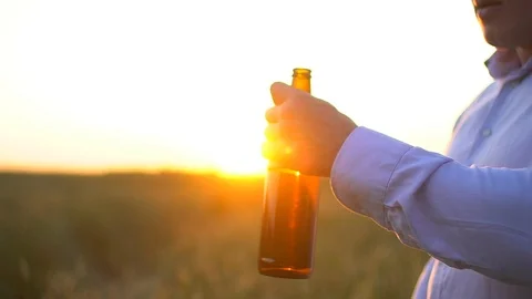 Man open a bottle of beer on background of the ripe wheat field at sunset. A man Stock Footage 97013577