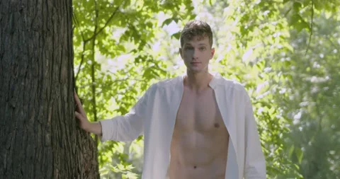 Man in an open shirt stands next to a large tree Stock Footage 237859086