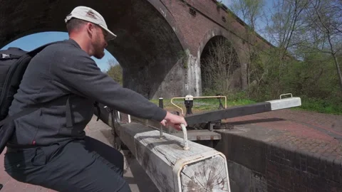 A man opening a canal lock under a railway bridge in the UK 库存影片 153904368