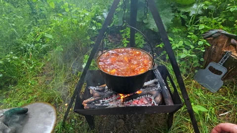 Man opening cauldron lid with boiling stew over campfire for outdoor campin.. 库存影片 342595446