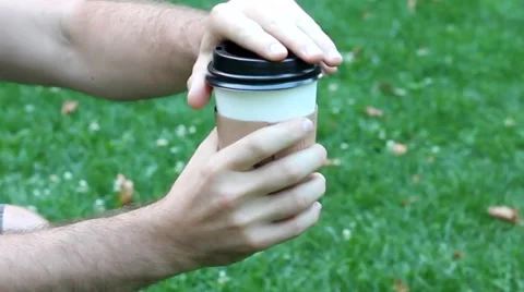 MAN IS OPENING THE COFEE CUP IN THE PARK ON GREEN GRASS OF LVIV UKRAINE Video stock 65416690