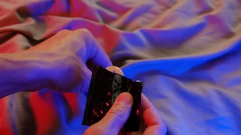 Man opening condom, close up. Hand holding a condom in package. Bedroom Stock Footage 295928355