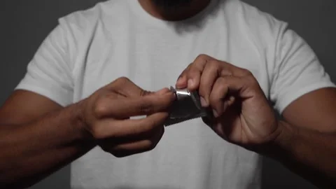 Man opening condom wrapper on gray background Stock Footage 314385014