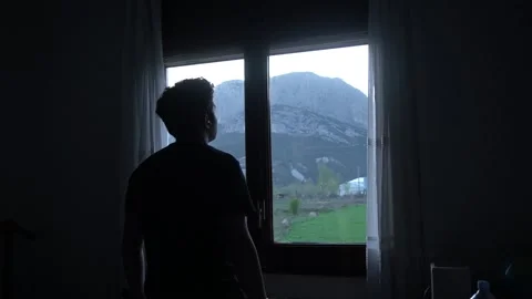 Man opening curtains in dark room and looking out the window Stock Footage