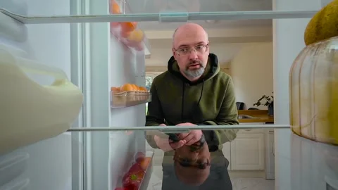 Man opening empty fridge and using phone with bored expression, view from inside Stock Footage 315463877