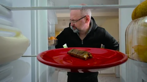 Man opening fridge, finding chocolate bar, taking bite and placing it back in Stock Footage 311455999