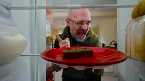 Man opening fridge, finding chocolate bar and devouring it greedily, view from Video stock 328369908
