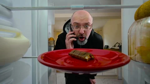 Man opening fridge while talking on phone, noticing bitten chocolate bar and Stock Footage 309021603