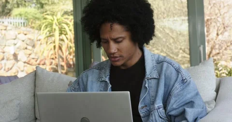 Man opening laptop and adjusting seat before typing on sofa by window with Stock Footage 341393349