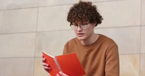 Man opening orange notebook, reading while frowning, tilting it, flipping pages 動画素材 340010013