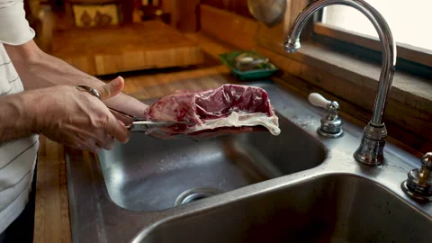 Man opening a piece of meat wrapped in plastic with a scissors over a sink Stock Footage 145998540