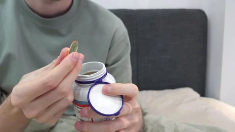 Man opening a pill bottle, taking out one soft gel capsule. Healthcare Stock Footage 284041897