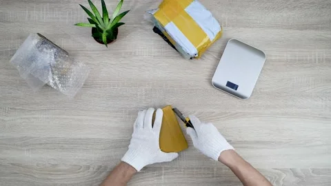 Man opening tiny parcel using knife. Unboxing procedure above view Video stock 147078577