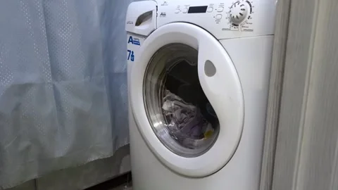 Man opens and closes door of front-loading washing machine inside bathroom at Stockbeeldmateriaal 340386642