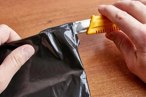 A man opens a black plastic envelope with a stationery knife. Foto stock