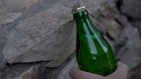 A man opens a bottle of carbonated drink hitting the curb. Glass bottle with Stock Footage 113214895