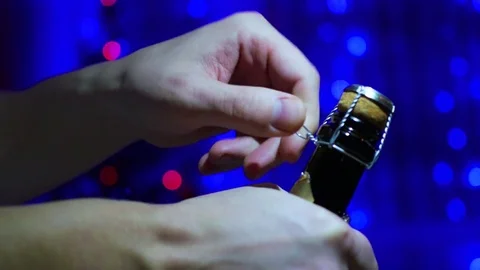 The man opens a bottle of champagne close-up. In the background, bokeh lights Video stock 71077993