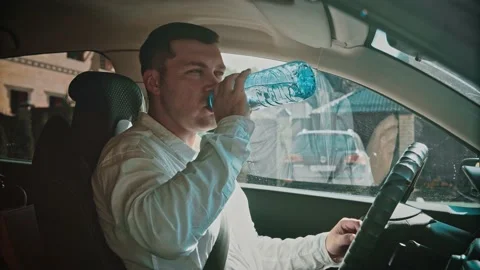 A man opens a bottle of water and drinks water while sitting in a car. Stock Footage 150122342