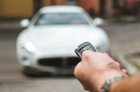 The man opens the car with a keychain, in the background is a white car. 스톡 사진