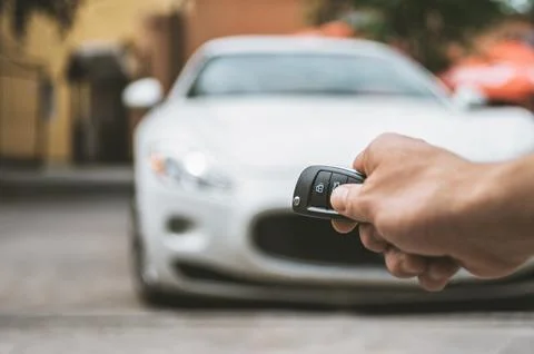 The man opens the car with a keychain, in the background is a white car. 스톡 사진