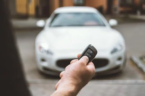 The man opens the car with a keychain, in the background is a white car. Stock Photos