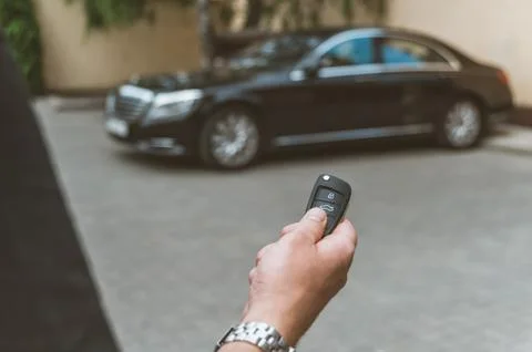The man opens the car with a keychain, in the background is a black car. 스톡 사진