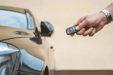 A man opens the car with a keychain, in the background is a yellow wall. 스톡 사진